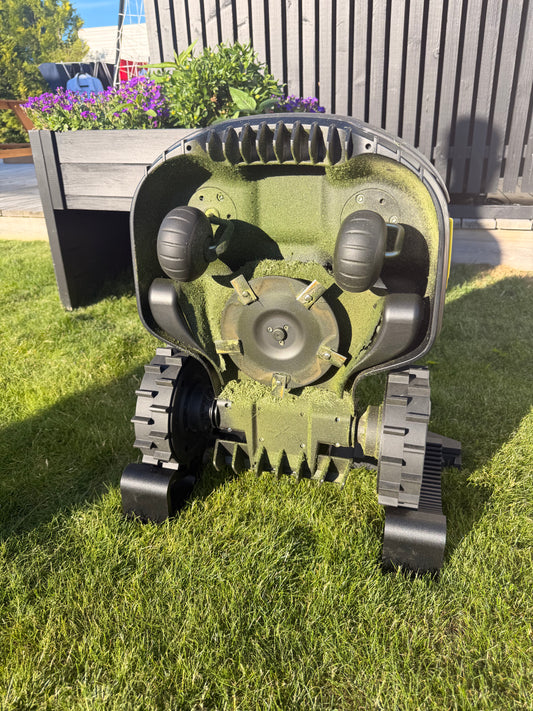Mammotion robot mower tilted up and held on the maintenance stand, exposing the underside and cutting blade disc for servicing and cleaning