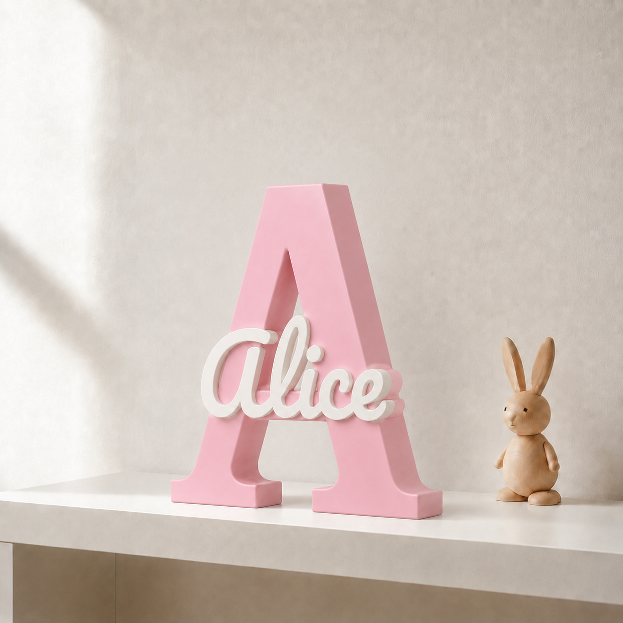 Pink 3D printed letter A name sign with the name Alice in white script, standing on a shelf