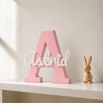 Pink 3D printed letter A name sign with the name Astrid in white script, standing on a shelf