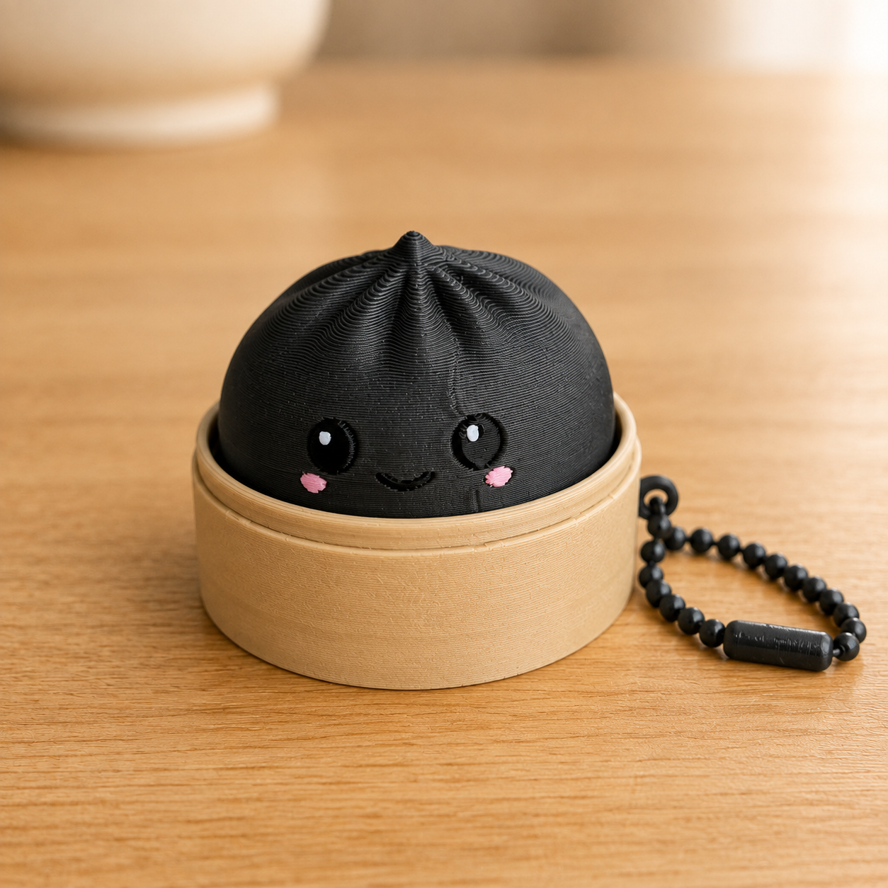Charcoal dumpling fidget clicker keychain in its bamboo steamer basket, with ball chain