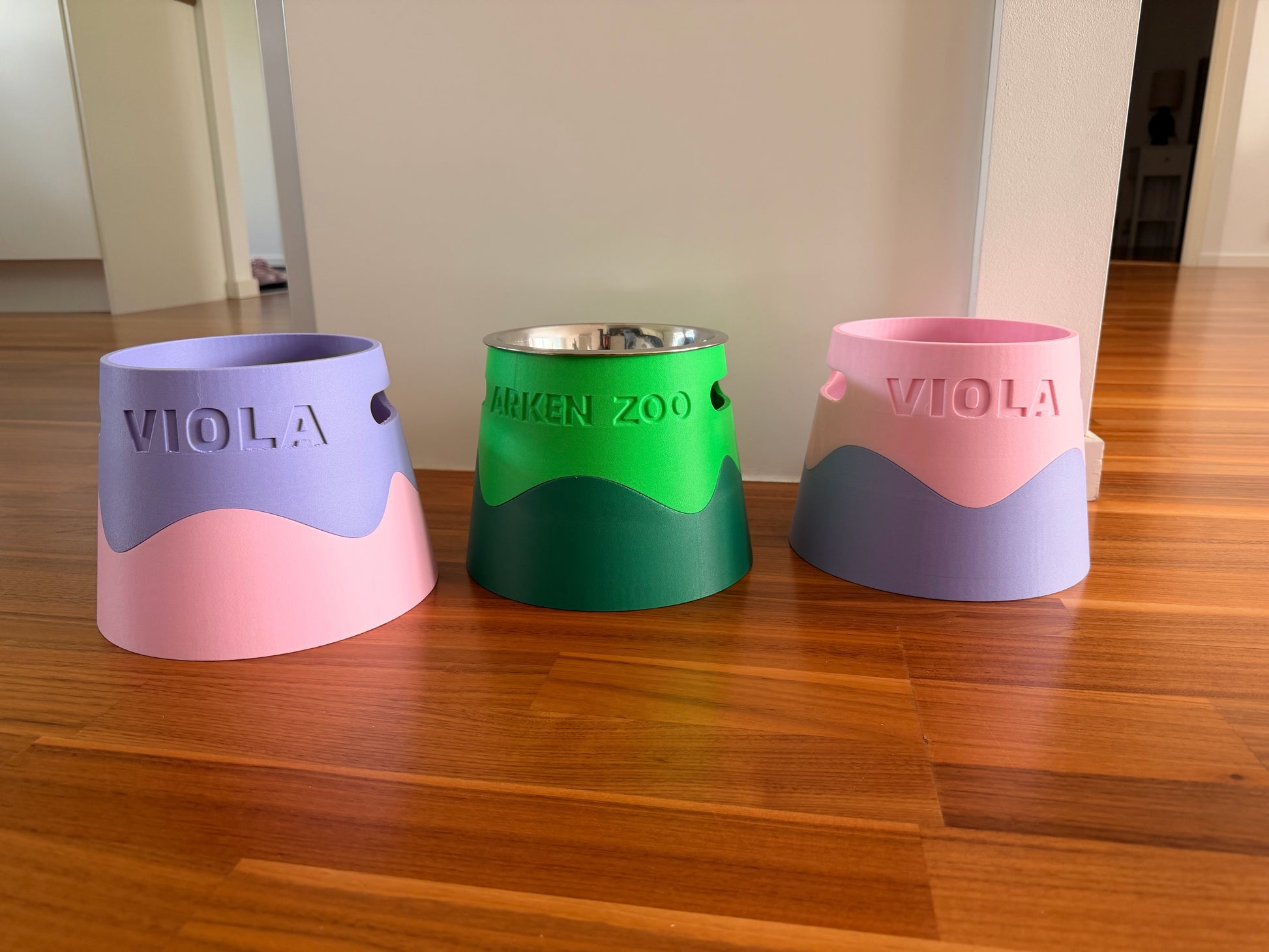 Three bowl stands side by side in lilac, green and pink, each with a name debossed on the side