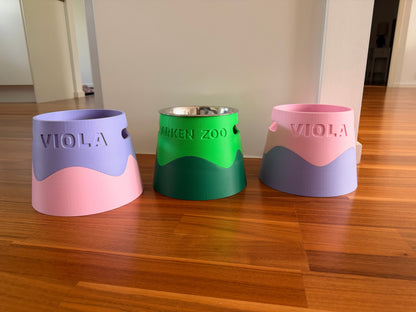 Three bowl stands side by side in lilac, green and pink, each with a name debossed on the side