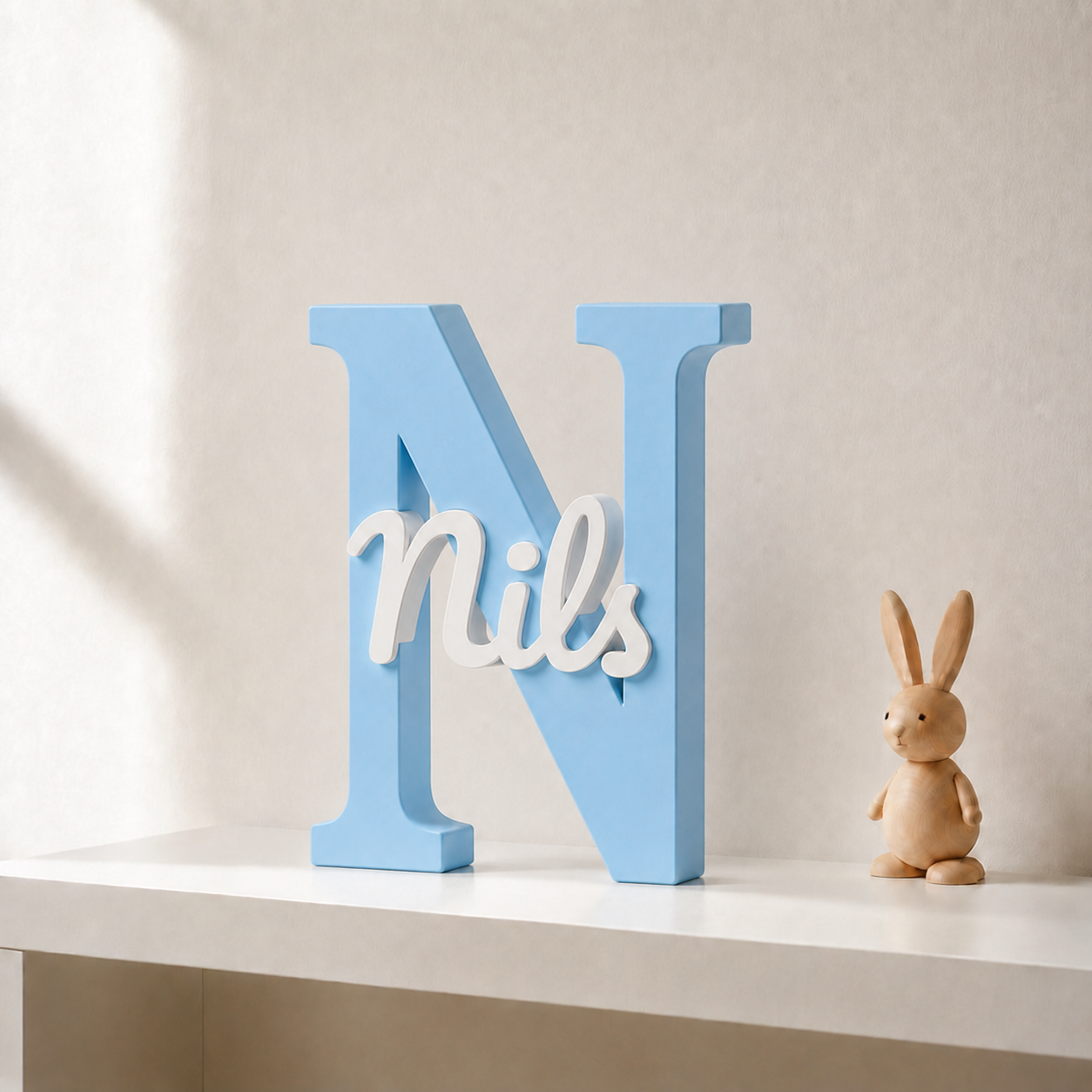 Light blue 3D printed letter N name sign with the name Nils in white script, standing on a shelf