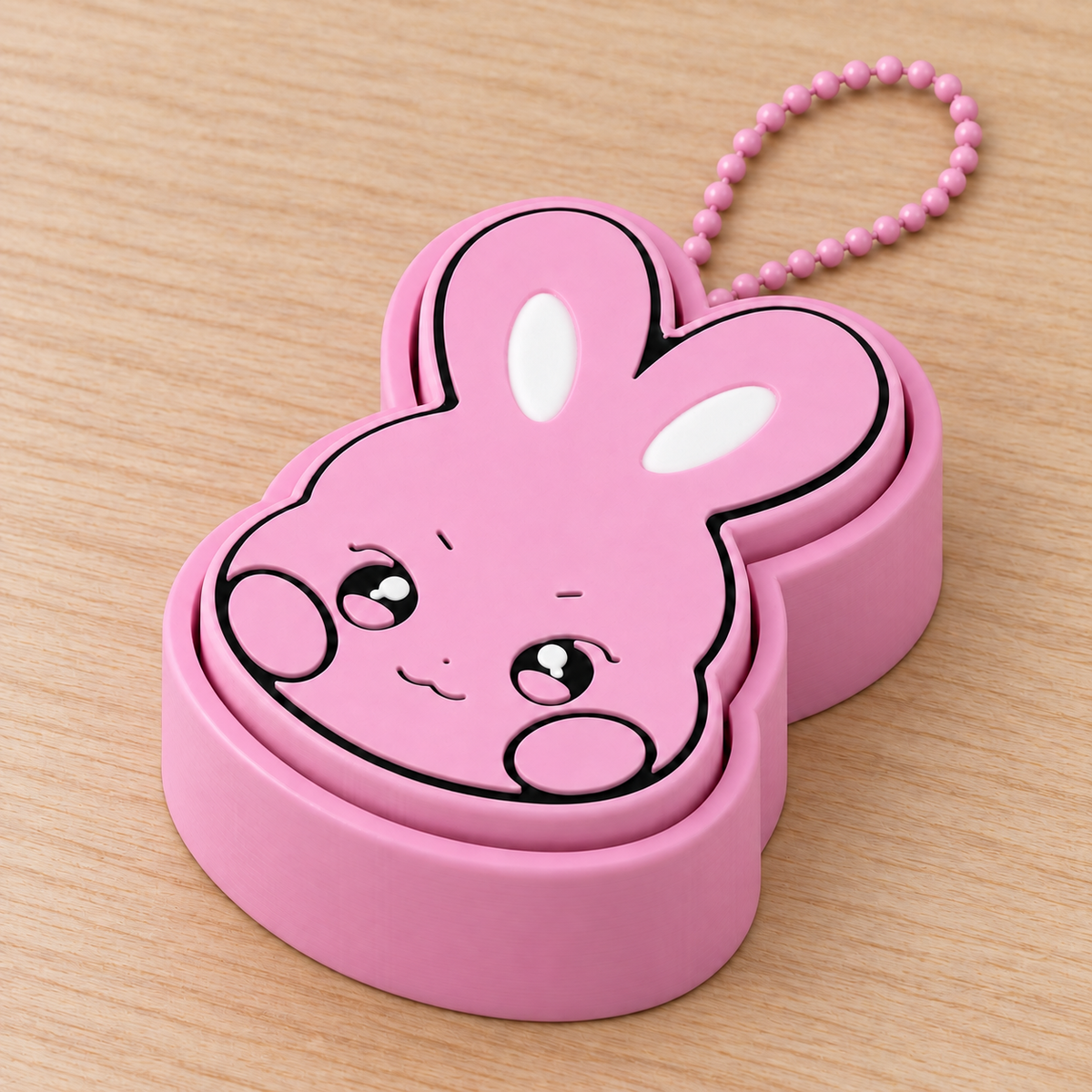 Pink DDEONGbyeoli rabbit clicker with a matching pink ball chain on a warm wooden tabletop, with the chain mounting point hidden behind the top of the base.