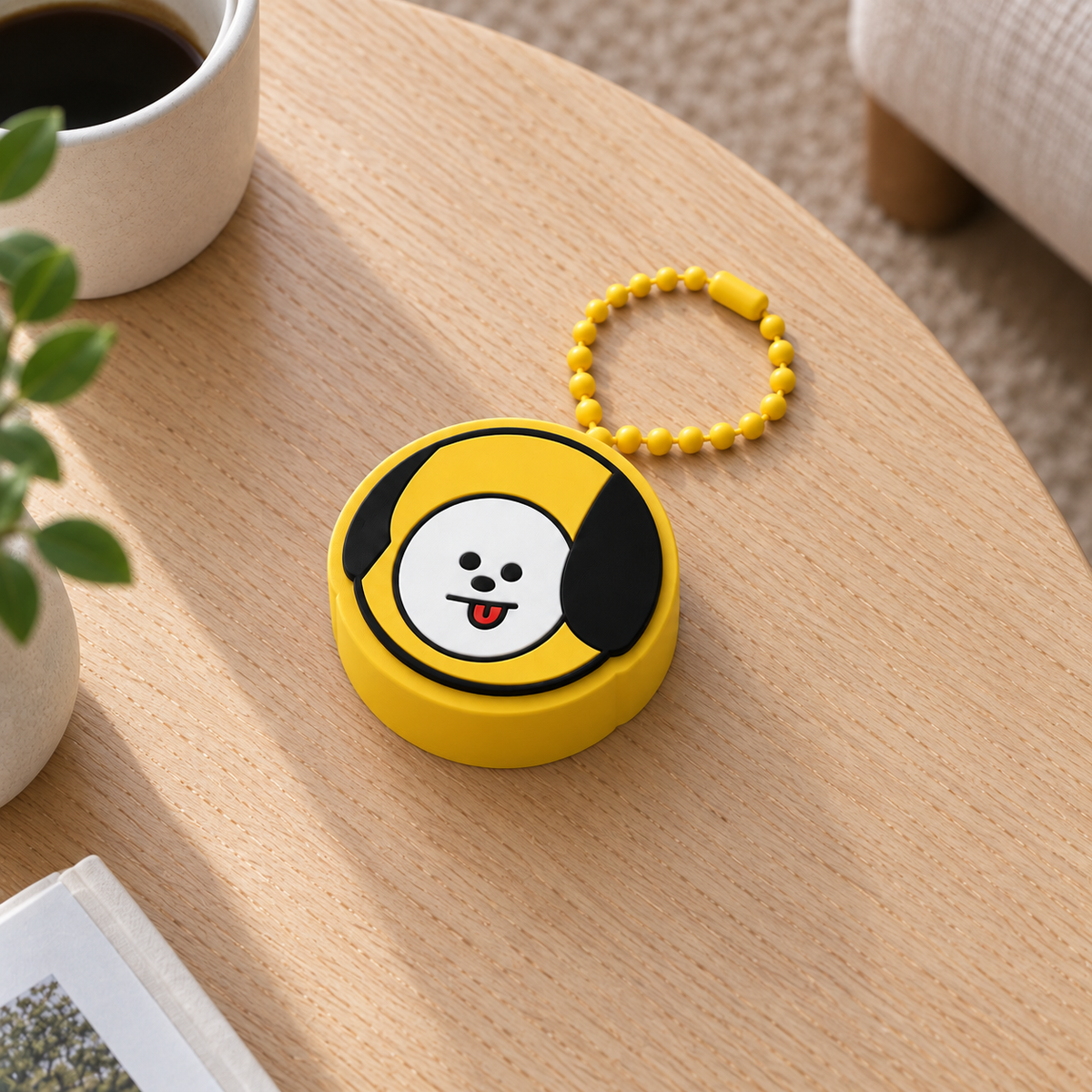 Yellow CHIMMY clicker with black ears, a white face and a yellow plastic ball chain on a light wooden table.
