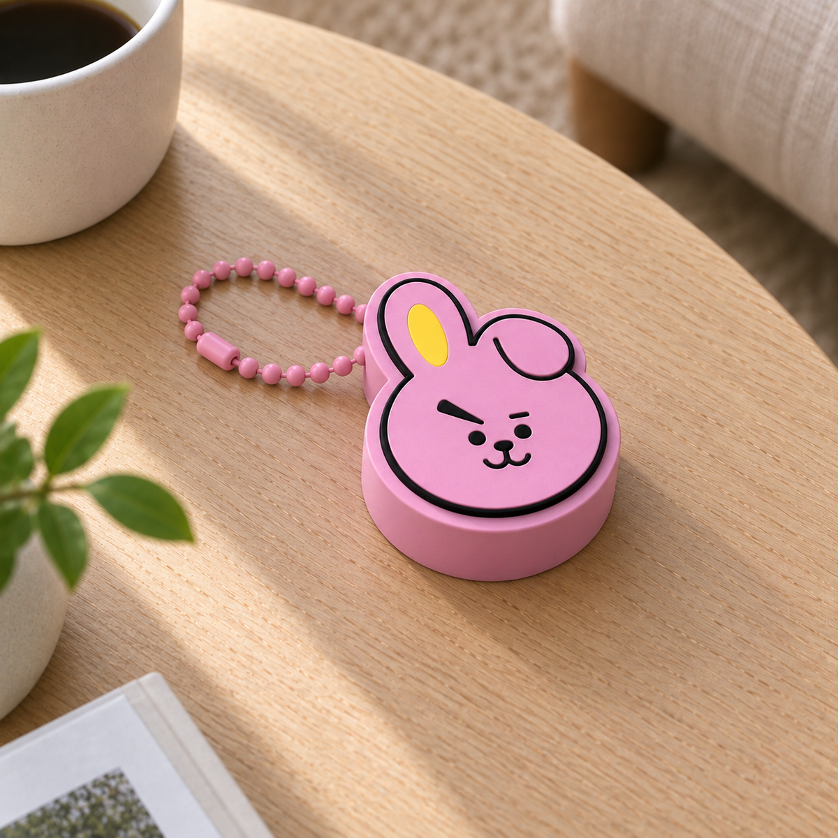 Pink COOKY bunny clicker with a yellow inner ear and a pink plastic ball chain on a light wooden table.