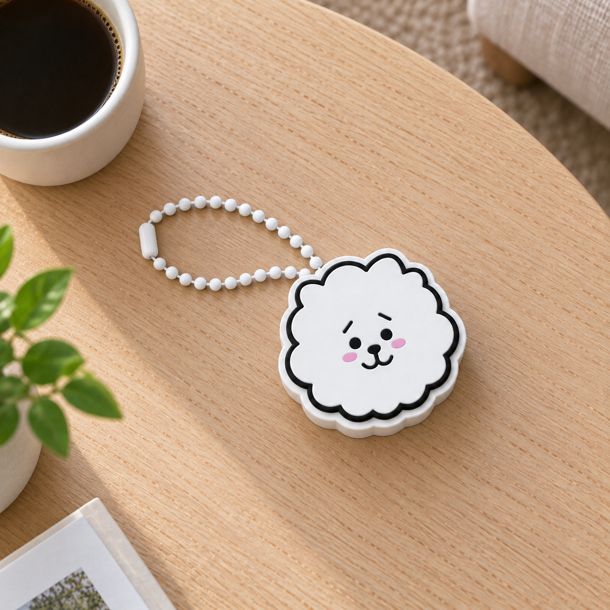 White RJ alpaca clicker with pink cheeks and a white plastic ball chain, viewed from above on a wooden table.