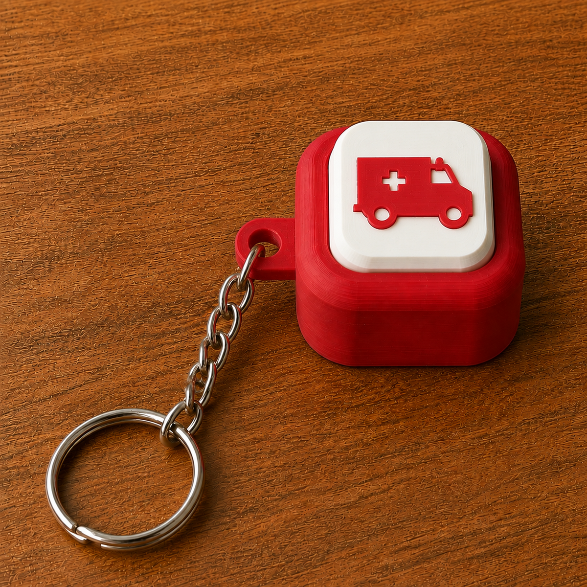 Red and white Hospital Clicker with a ambulance design, raised white button, side loop, metal chain and split ring on a wooden surface.
