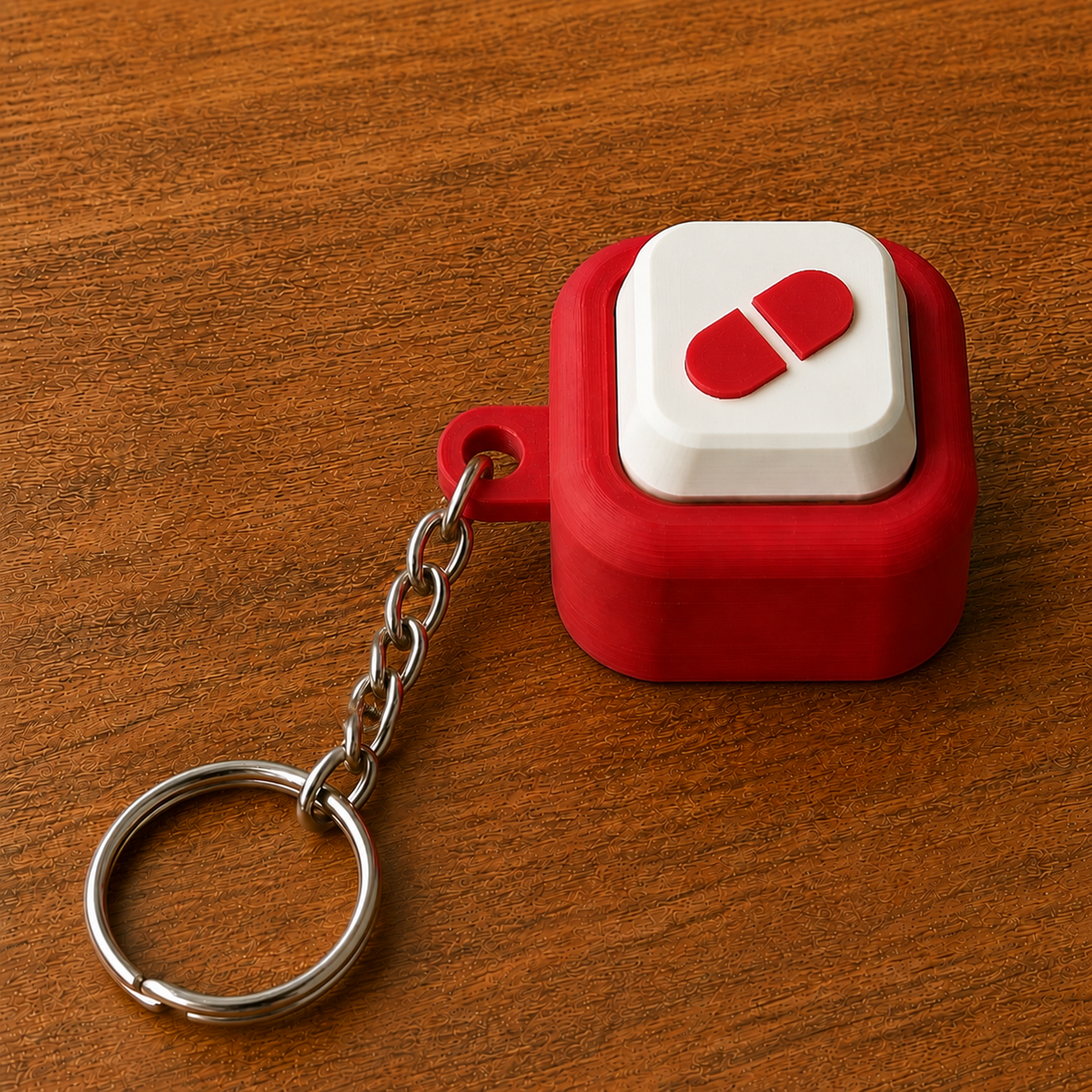 Red and white Hospital Clicker with a capsule design, raised white button, side loop, metal chain and split ring on a wooden surface.