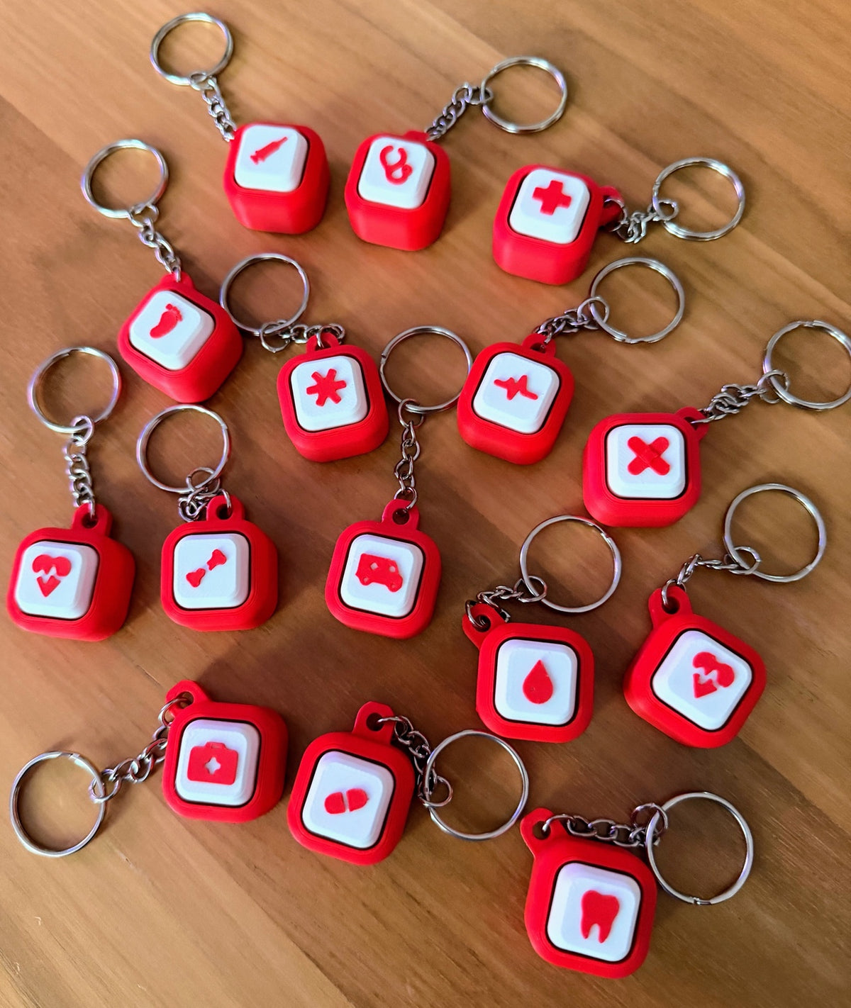 Red and white Hospital Clicker keychains with metal rings and chains, photographed at an angle on a wooden table.