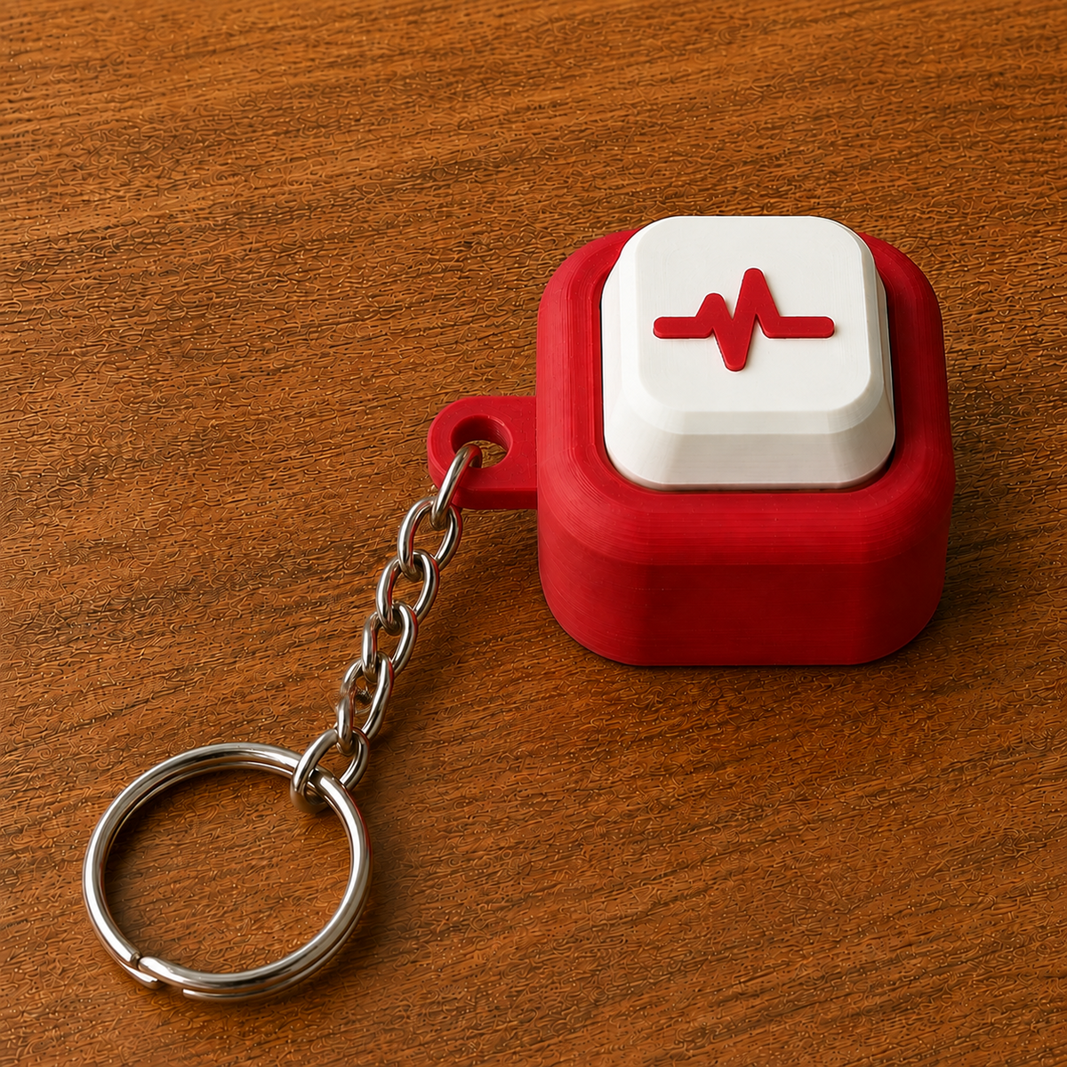 Red and white Hospital Clicker with a pulse line design, raised white button, side loop, metal chain and split ring on a wooden surface.