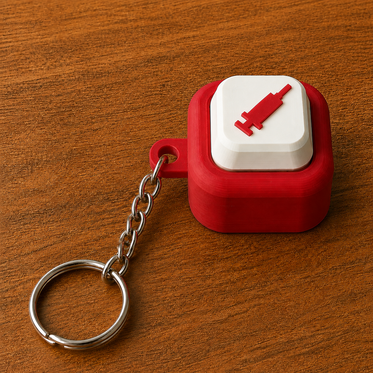 Red and white Hospital Clicker with a syringe design, raised white button, side loop, metal chain and split ring on a wooden surface.