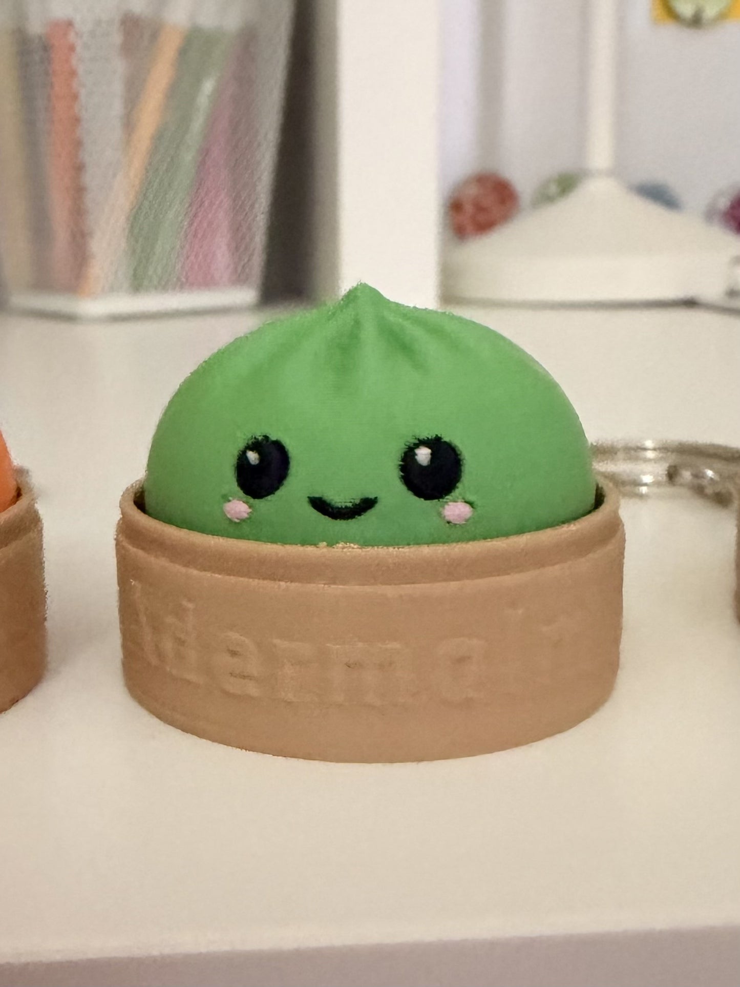 Green dumpling fidget clicker keychain in embossed Adermalm steamer basket, close-up