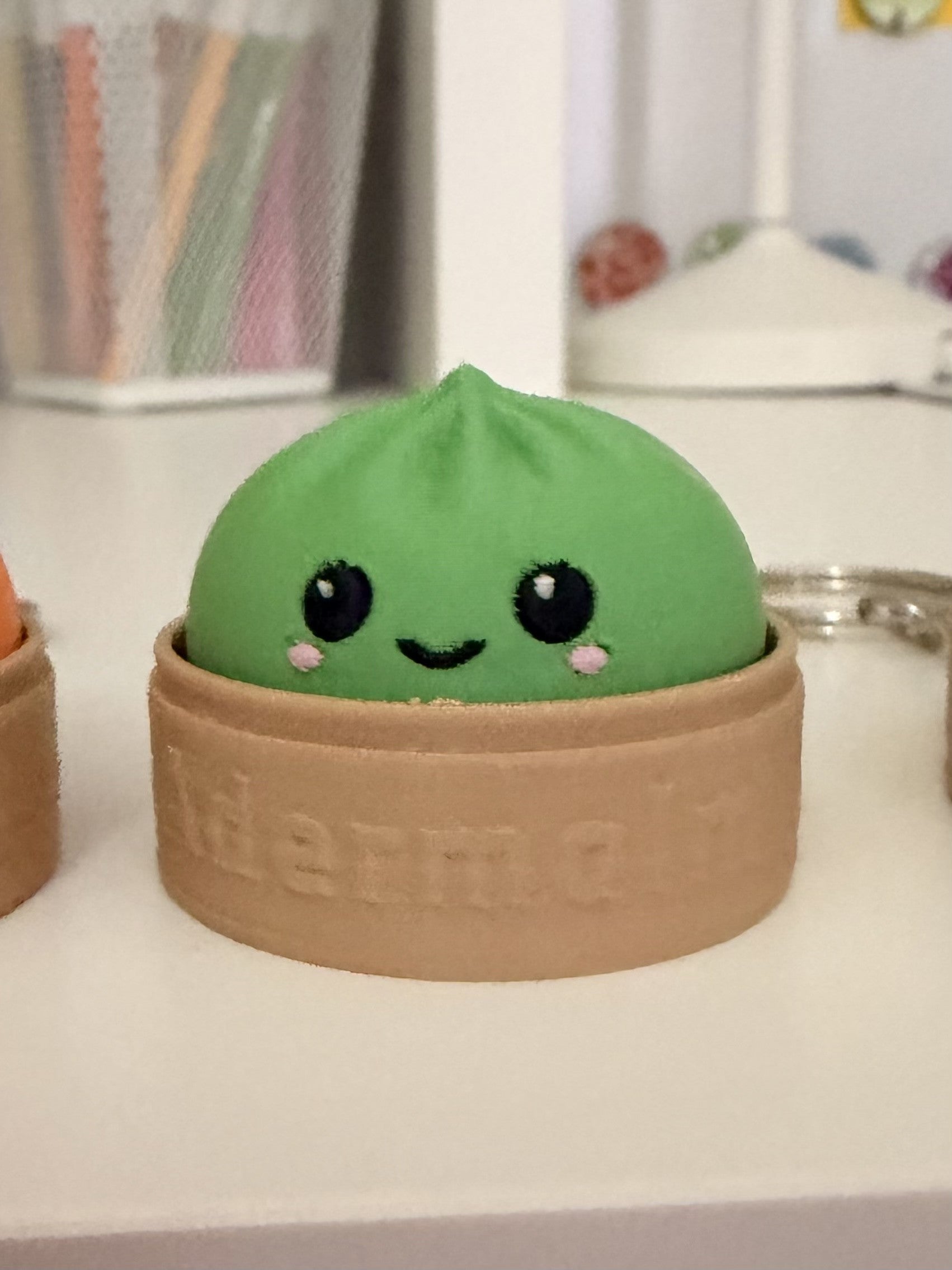 Green dumpling fidget clicker keychain in embossed Adermalm steamer basket, close-up